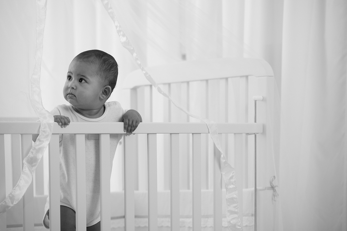 Curious baby standing in pink crib, looking curiously away.
